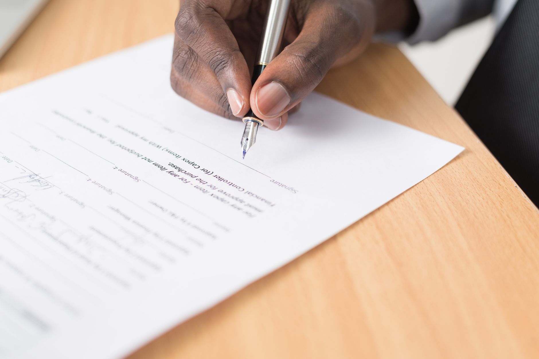 A hand signing a sheet of paper on a desk.