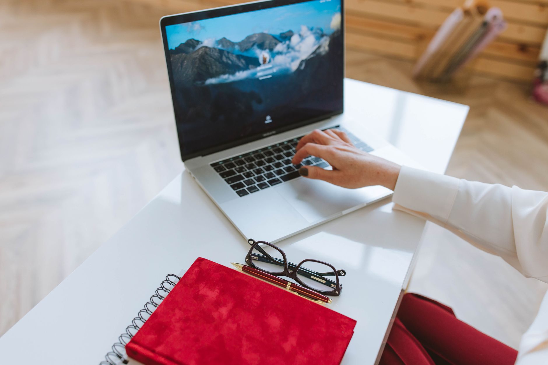 A desk planner, a notebook and a laptop on a desk.