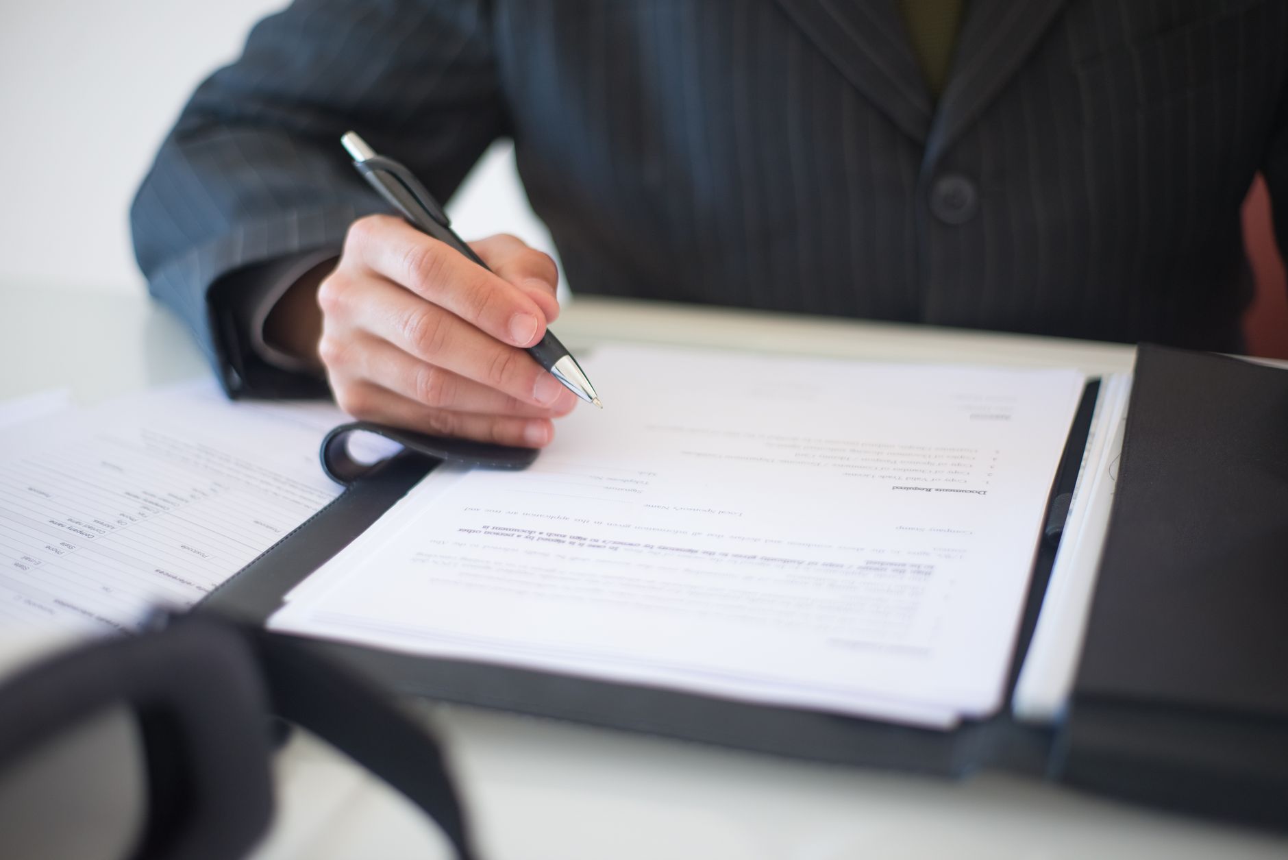 A hand holding a pen over a contract on a desk.