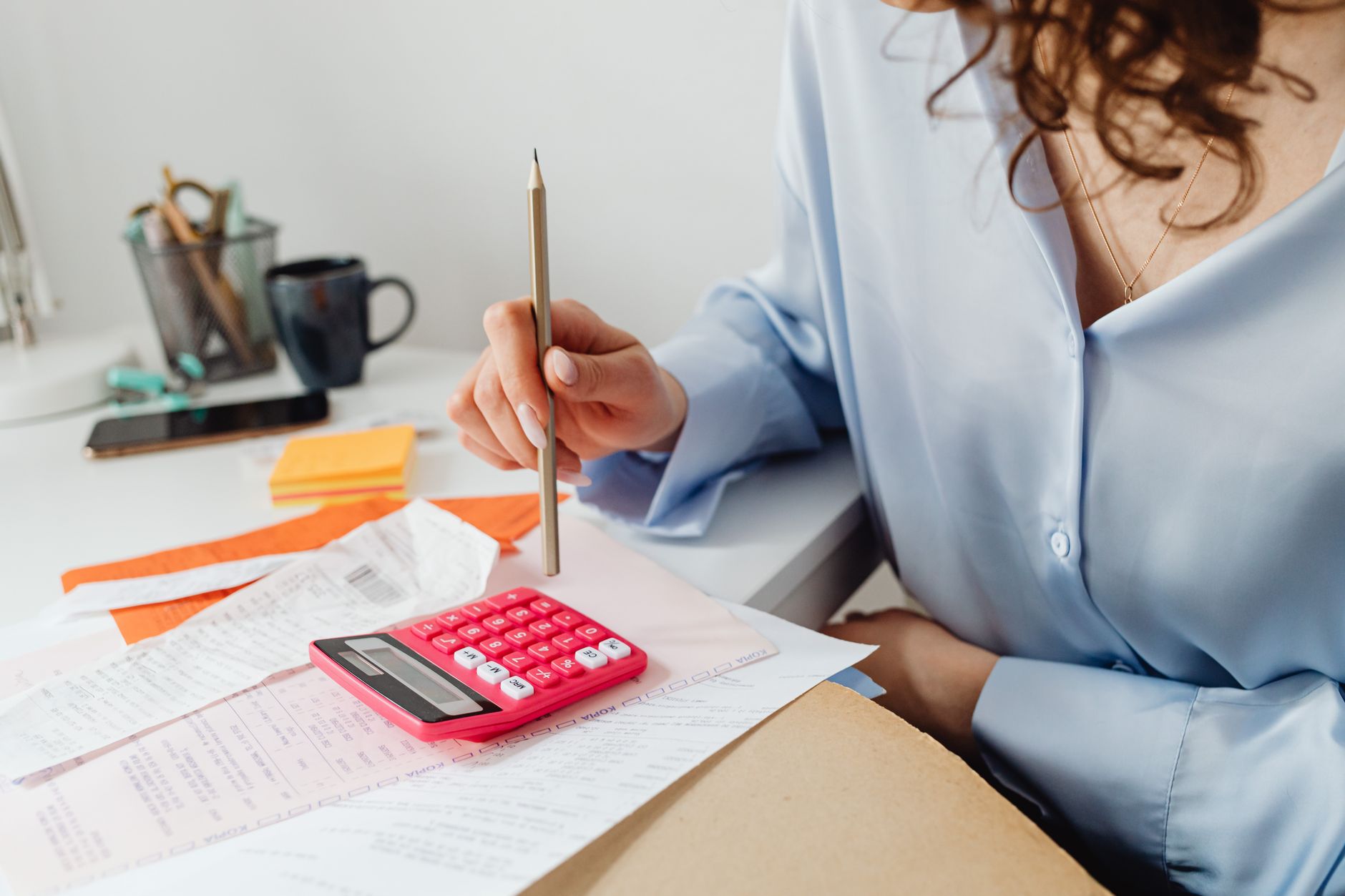 A calculator and a stack of printed invoices on a desk in daylight.