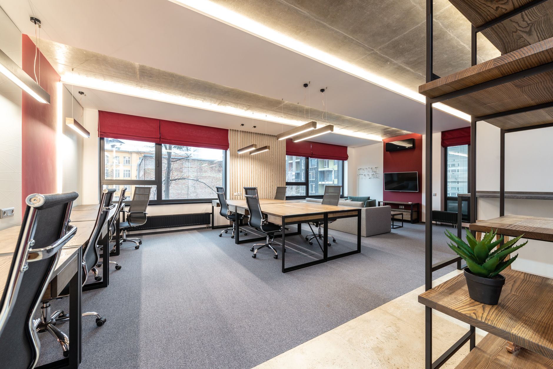 A bright empty office room with desks and chairs beside large windows.